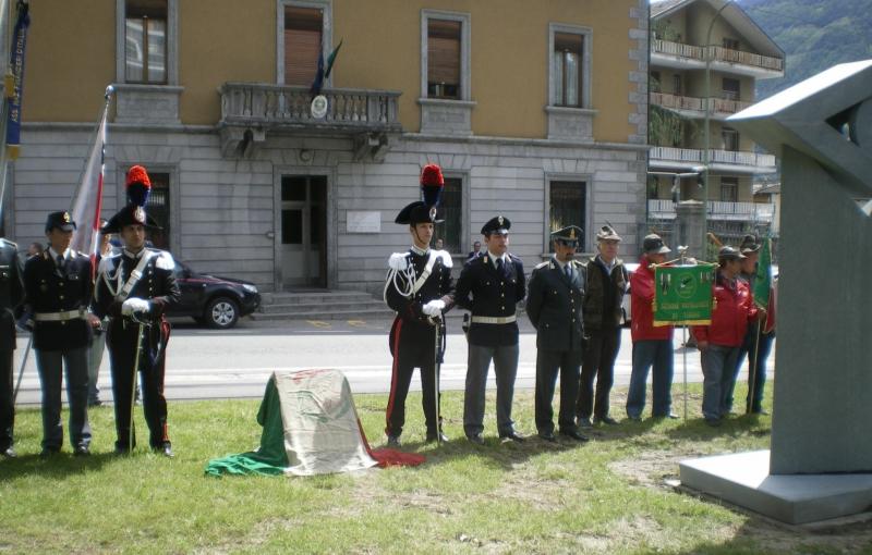 Carabinieri, Finanzieri e agenti della Polizia di Stato schierati a guardia d'onore presso il cippo dedicatorio. 
A sinistra si
